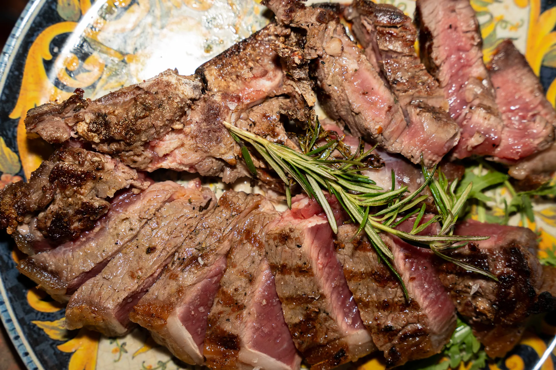 Bistecca alla Fiorentina tagliata e cotta alla brace, con segni di griglia e rosmarino, servita su piatto in ceramica toscana — All You Can Steak Sesto Fiorentino