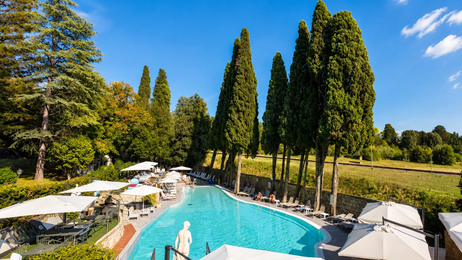 Piscina dell'Hotel Fantastic Garden con acqua turchese, ombrelloni bianchi, una statua classica e un filare di cipressi, accanto ad All You Can Steak a Sesto Fiorentino